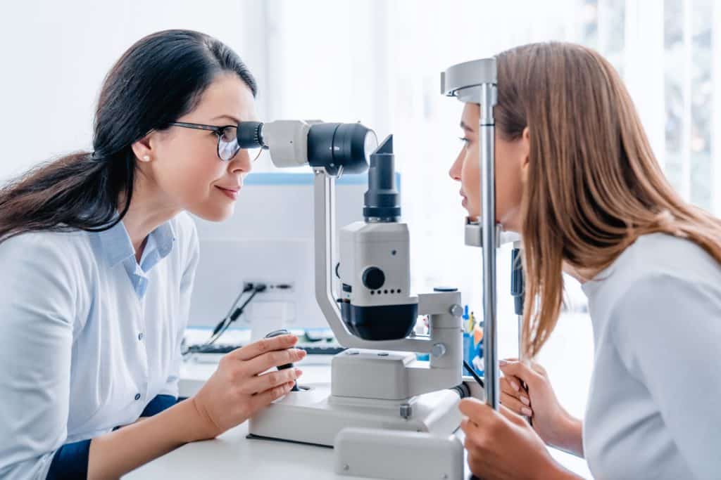Adult female doctor ophthalmologist checking eye vision of young girl in modern clinic